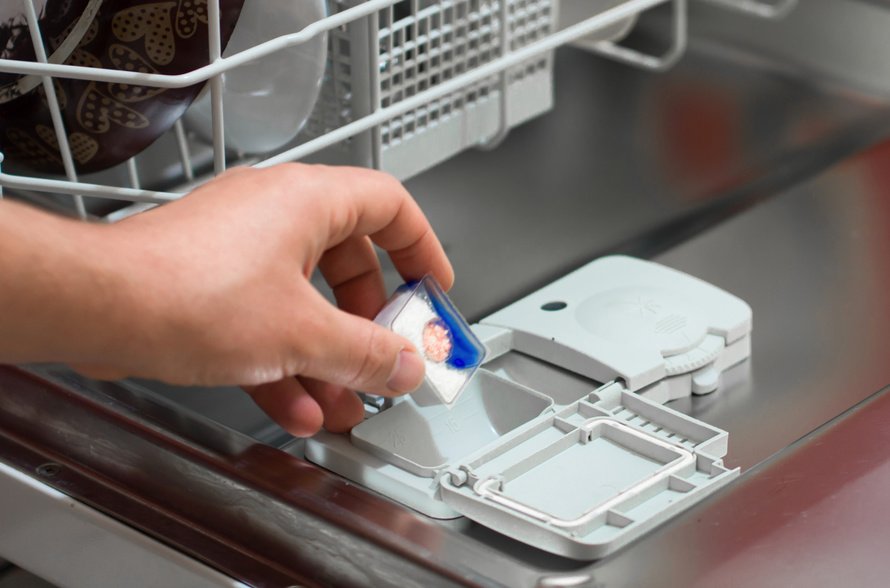 person placing dishwasher detergent packet in dishwasher